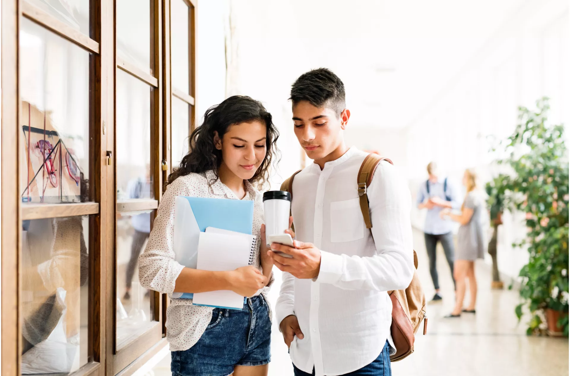 Two coming-of-age Latino students in a school setting looking at their phone. 