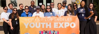 Youth Development Department staff at the 2023 Youth Expo behind a banner. 